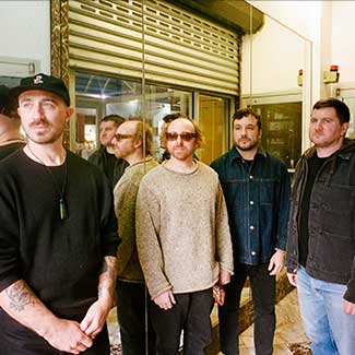 Die Band steht zusammen mit dem Rücken zu einem Spiegel