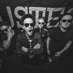 Die Band Buster Shuffle schaut ernst, trägt Sonnenbrillen und steht vor einer Wand