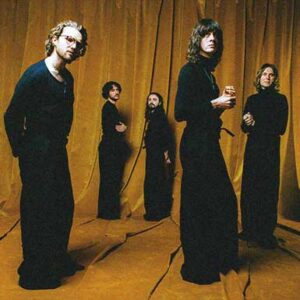 Die Band Blossoms steht in schwarz gekleidet vor einem senffarbenen Vorhang