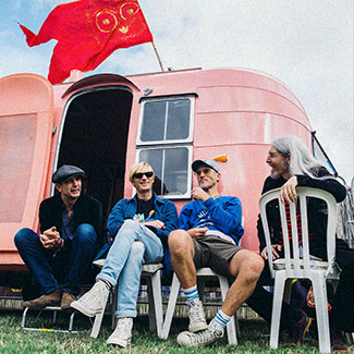 Kula Shaker sitze vor einem rosfarbenen Campingwagen