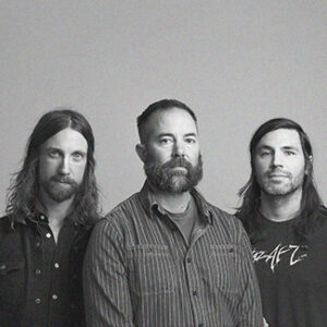 Die drei Musiker von Russian Circles stehen zusammen und schauen in die Kamera vor einem neutralen Hintergrund