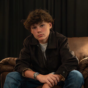 Porträt von Maddox Batson. er sitzt auf einem Sessel, Unterarme auf den Knien abgestützt und blickt in die Kamera