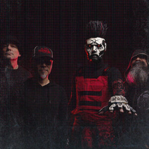 Bandfoto von Static X: vier Musiker vor schwarzem Hintergrund, Sänger mit Maske streckt die Hand nach vorn