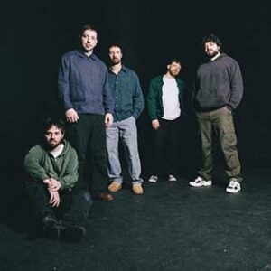 Die Band steht zusammen vor einem schwarzem Hintergrund